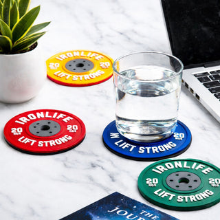 Colourful weight plate style coasters with “Ironlife Lift Strong” design, novelty gym gift for fitness lovers on desk with glass of water