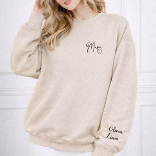 Woman wearing a beige sweatshirt with ‘Mum’ and a heart on the chest, and personalized names ‘Olivia’ and ‘Liam’ on the sleeve