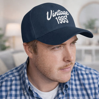 Man wearing a navy blue baseball cap with year of birth text, paired with a blue checkered shirt, looking to the side