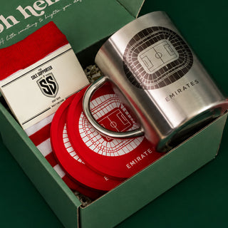 Emirates football-themed gift set in a green box, featuring a stainless steel mug with a stadium graphic, red coasters, a red-and-white striped knit sock, and a branded card.
