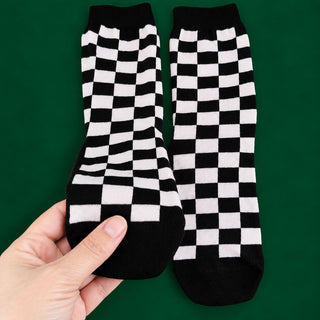 A pair of black and white checkerboard crew socks held up by a hand against a solid green background.
