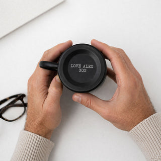 Person holding a black metal mug with  engraved text on the base of the mug