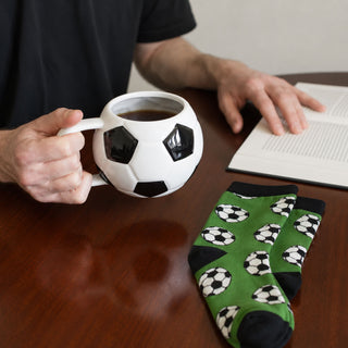 Man holding a football-shaped mug with matching green football socks on a wooden table