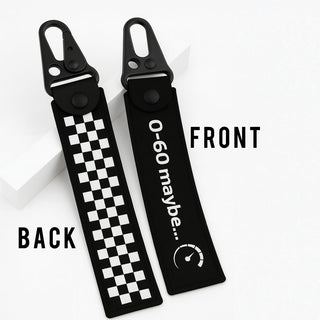 Two black car keychain fobs shown on a white background, labeled BACK and FRONT. The back side features a black and white checkerboard pattern, and the front side is black with white text reading '0-60 maybe.