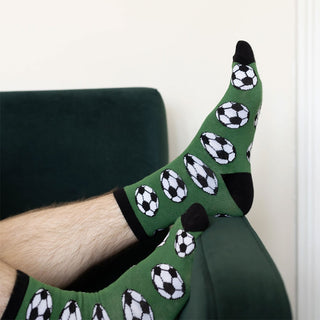 Green football print socks worn while relaxing on a sofa