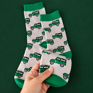 A pair of white crew socks with green cuffs, heels, and toes, featuring an all-over print of land rovers, held up by a hand against a dark green background.