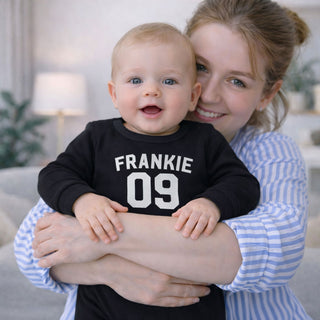Baby wearing personalised black football style baby grow with name and number, stylish newborn outfit