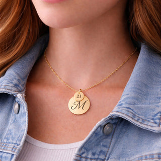 Close-up of personalised gold disc necklace with engraved initial M and 21 charm worn by young woman