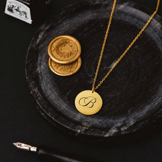 Personalised gold disc necklace with engraved letter pendant displayed on dark styling plate