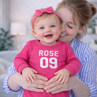 Baby girl wearing personalised pink football style baby grow with custom name and number, ideal baby gift