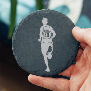 Round slate coaster with a personalised engraved silhouette of a runner and text, held by a hand.