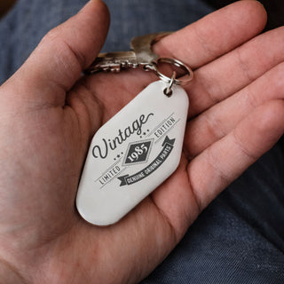 Personalised stainless steel motel style keyring with vintage birth year design held in hand, custom retro birthday keychain gift
