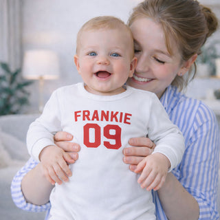 Baby wearing personalised white football style baby grow with custom name and number, perfect newborn gift