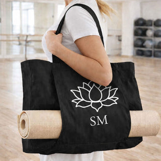 Black personalised yoga mat tote bag with lotus design and initials "SM", carried over shoulder with rolled yoga mat in a bright studio
