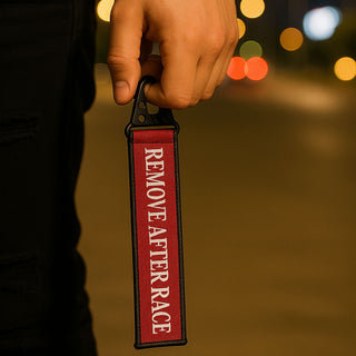 Red Remove After Race keychain inspired by Formula 1 motorsport, held in hand at night
