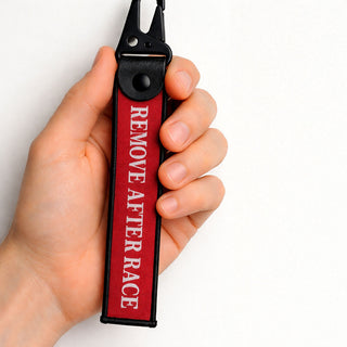 Hand holding a red Remove After Race keychain inspired by Formula 1 motorsport on a white background